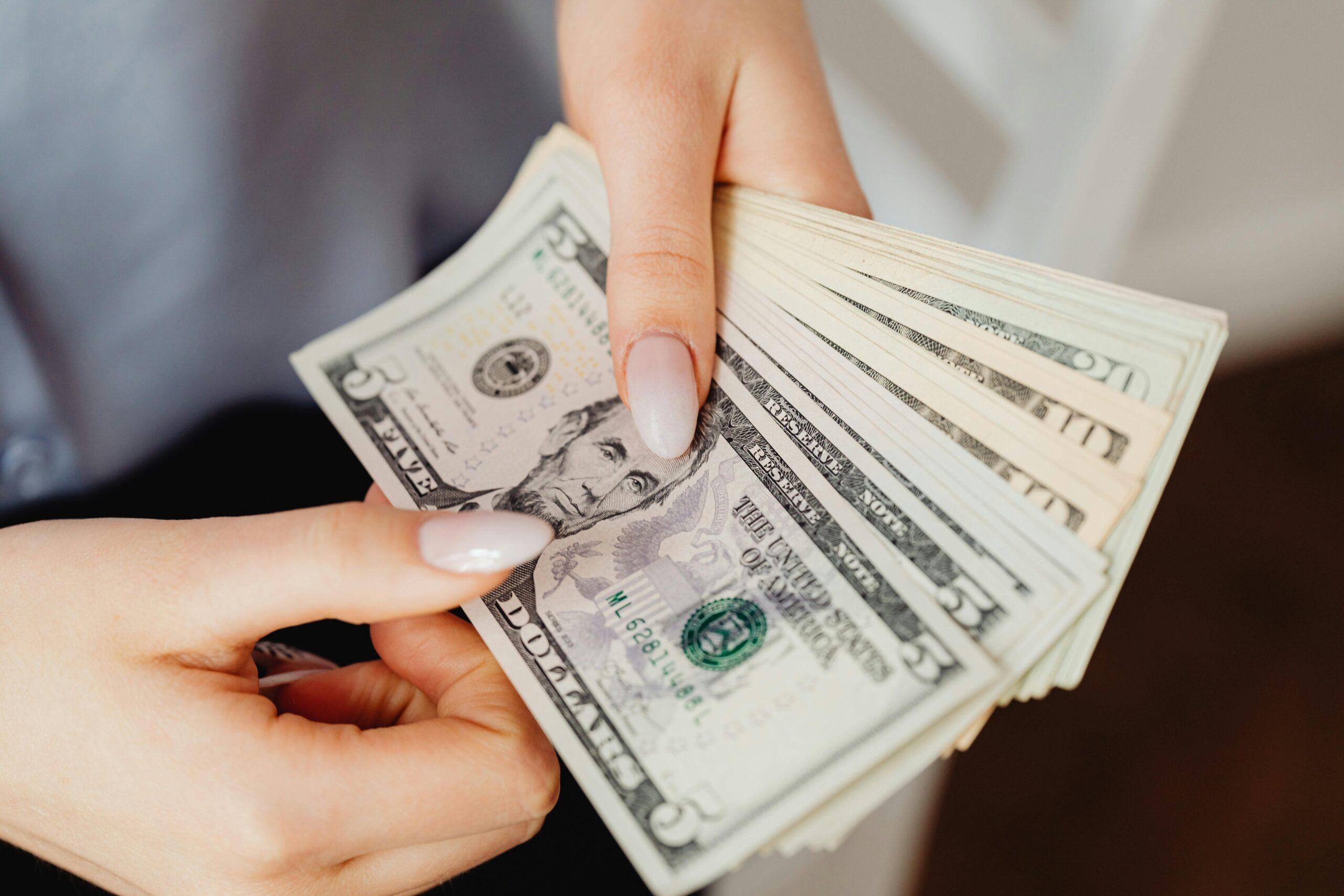 Hands count US dollar bills, showcasing finance and cash handling concepts.